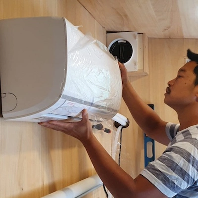 You-Liang installe la pompe à chaleur Airton sur le mur en bois de la tiny house Youca